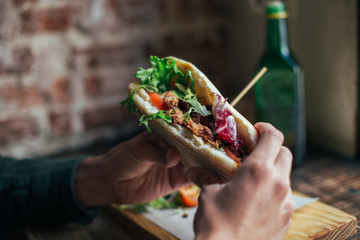 Person holds big tasty sandwich with crispy tandoori chicken and green salad at cool and trendy downtown food joint or restaurant cafe. Healthy lunch break