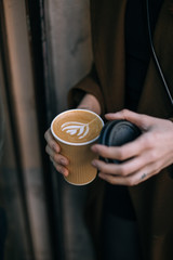 Trendy cool hipster woman or young girl with millennial tribal tattoos on fingers and hands holds take away to go cup of coffee with milk latte art, concept life on the go, warm and cosy drink