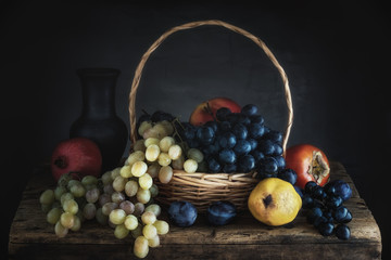 Still life with grapes in a basket and pear, prune, pomegranate and persimmon on a wooden village table on a gray background. Vintage. Low key. Focus concept.