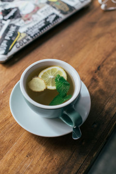 Blue cup on plate of hot steaming ginger mint tea or infusion with organic honey, calm and soozing warm beverage. Concept of winter morning at cafe or coffee shop