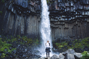 man tourist photographing on smartphone Svartifoss waterfall surrounded by basalt columns in the...