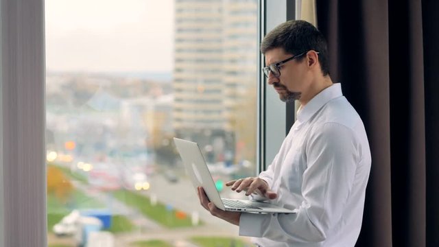 A pensive businessman uses a laptop near a window. 