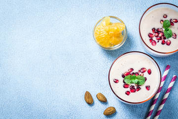 Obraz na płótnie Canvas Greek yogurt pomegranate mandarin smoothie on light blue background. Winter fruit healthy dessert. Top view, copy space.