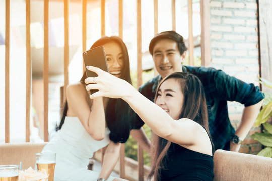 Group of asian smiling friends taking funny selfie in restaurant.