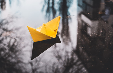 Yellow paper boat in a city street puddle. Autumn optimism