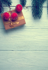 Christmas background. Branches of a Christmas tree, small red apples and gift box on a white wooden background.