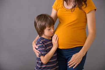 Little child, boy, hugging his pregnant mother at home, isolated image