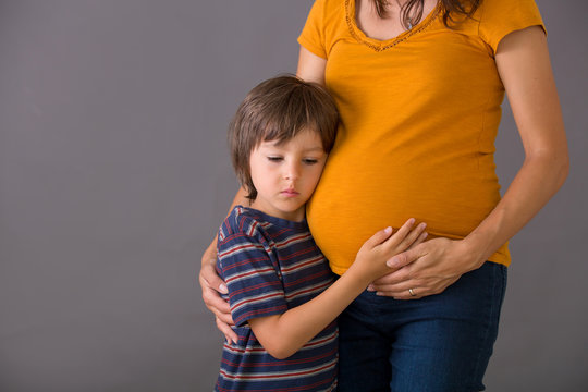 Little child, boy, hugging his pregnant mother at home, isolated image