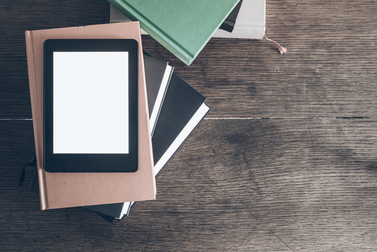 e-reader on stack of books on rustic wooden desk
