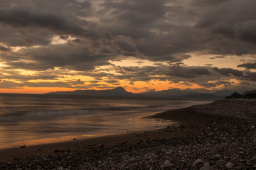 Fototapeta na wymiar Paesaggio mare , spiaggia al tramonto. Cielo colorato e montagne in background. 