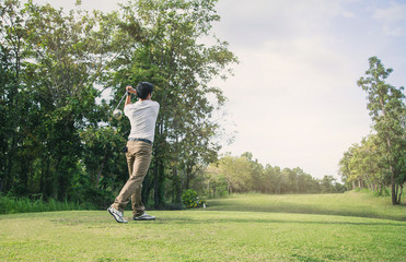 Man playing golf on a golf course in the sun.Golfer hitting golf shot with club on course .