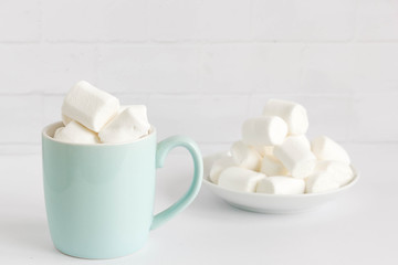 Fototapeta na wymiar White marshmallows in green mug and on white plate. Traditional winter sweet still life.
