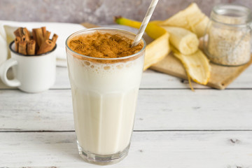 Banana oat milkshake with cinnamon on top, served on wooden table