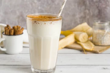 Foto op Plexiglas Milkshake Banaan haver eiwitshake met kaneel en papierstro in een glas.