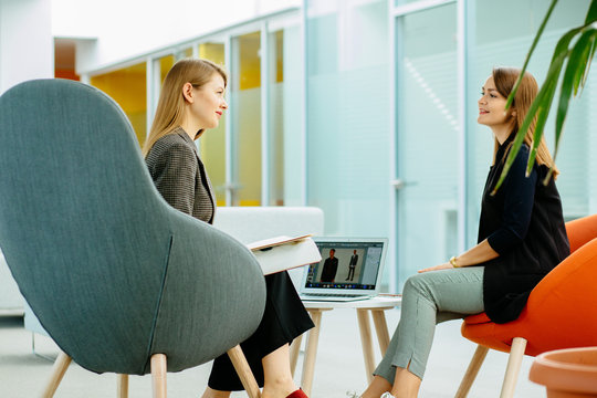 Team work process. Two women with laptop sitting in front of each other in open space comfortable office. Business, work and people concept.