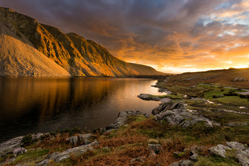 Golden evening light illuminating mountain at Wastwater in the English Lake District with moody dramatic clouds.