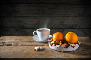 Christmas cookies and oranges in a bowl and a cup with hot coffee on a rustic table, dark wooden...