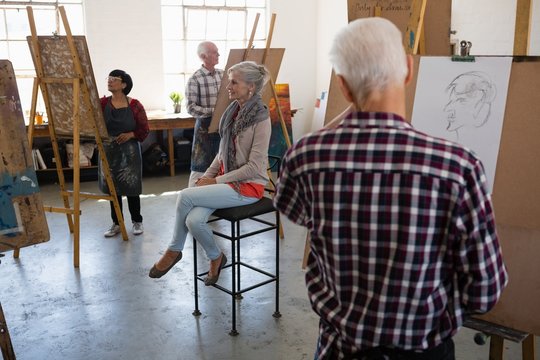 Senior woman sitting on chair while artists sketching on paper