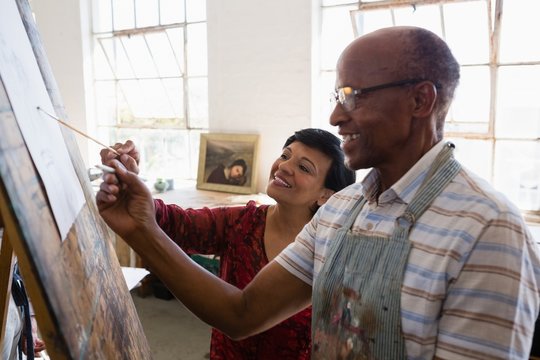 Smiling woman assisting male friend while painting