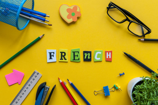 FRENCH - word made with carved letters on yellow desk with office or school supplies, stationery. Concept of Franch language courses
