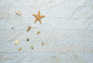 Fototapeta na wymiar Conchas, estrella de mar y caracolas marinos sobre fondo de madera azul con red de pescar