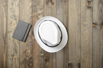 Sombrero blanco y libreta negra sobre fondo de madera