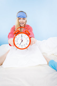 Sleepy woman wearing pajamas holding clock