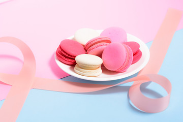 Homemade Colorful macaroons or macaron on White plate with pink ribbon on pink and blue pastel background