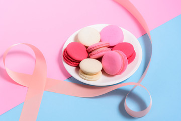 Homemade Colorful macaroons or macaron on White plate with pink ribbon on pink and blue pastel background