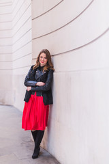 Fototapeta premium The young elegant smiling woman standing outdoor and relying on the wall