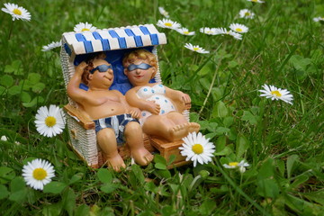 Mann und Frau liegen entspannt in einem Strandkorb auf einer grünen Wiese mit Gänseblümchen

