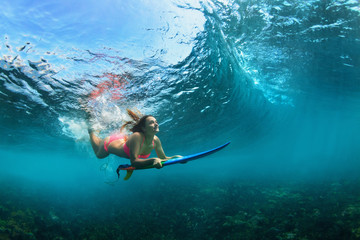 Active girl in bikini in action. Surfer woman with surf board dive underwater under breaking big wave. Teenage lifestyle. Water sport, extreme surfing in adventure camp on family summer beach vacation