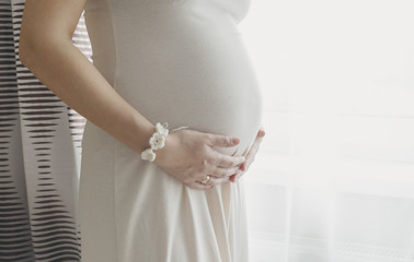 Pregnant woman holding belly standing near the window