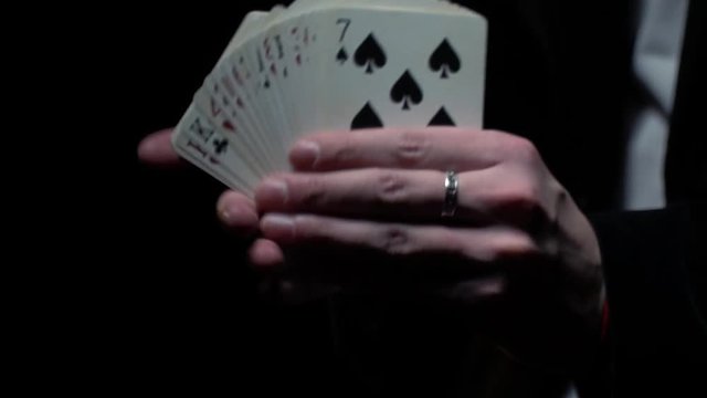 The magician in a black jacket shuffles a deck of cards, slow motion