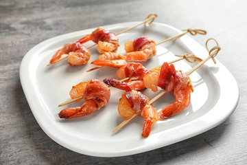 Plate with skewered shrimps wrapped in bacon on table