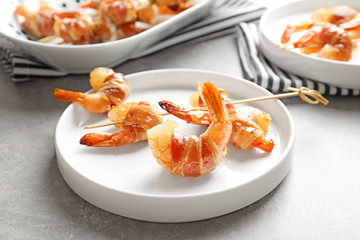 Plate with skewered shrimps wrapped in bacon on table