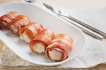 Ceramic plate with bacon wrapped chicken nuggets on table