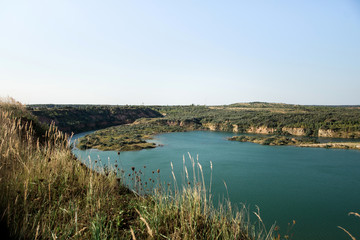 Landscape of an old flooded industrial granite quarry filled with water. Lake on the background of rocks and fir trees.