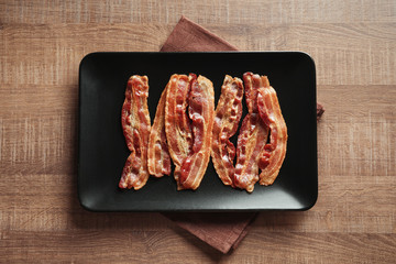 Plate with cooked bacon rashers on table