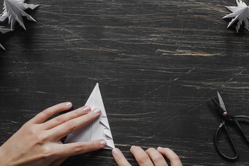 Three white paper Christmas trees with scissors on black wooden table with hands