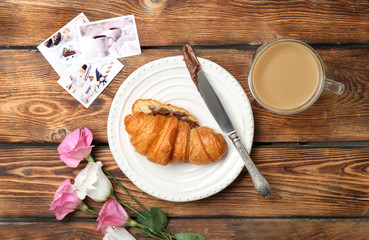 Composition with tasty croissant, coffee and flowers on wooden table