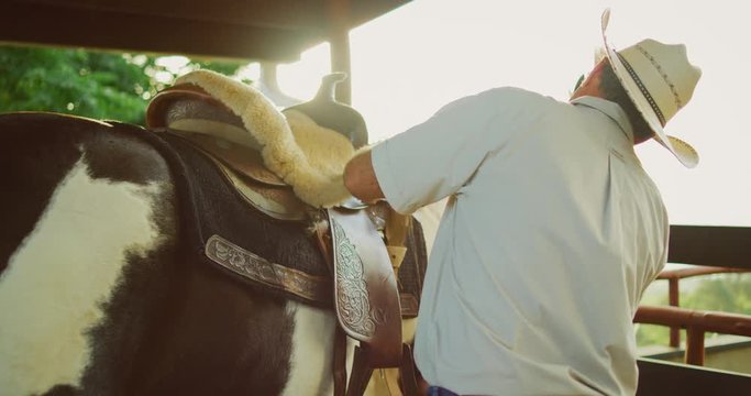 Cowboy adjusting the saddle on his horse to go riding