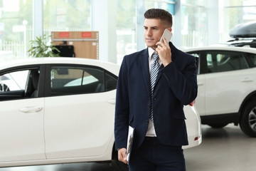 Salesman talking on mobile phone in car salon