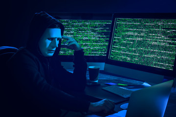 Hacker in mask using computer in dark room