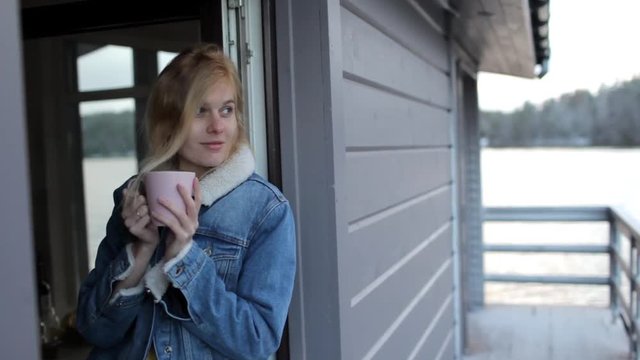 girl is drinking coffee while sitting on a window of a house on the water