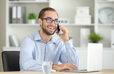 Attractive man with laptop talking on phone in office