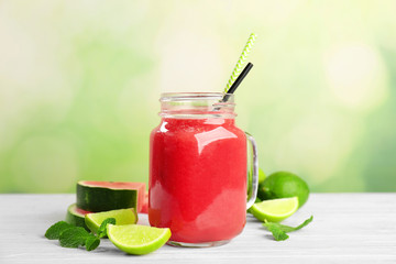 Mason jar with fresh watermelon smoothie on table against color background