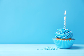 Tasty cupcake with candle on table against color background