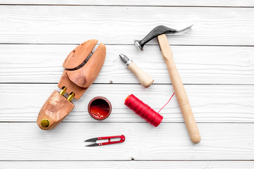 Shoe repair. Wooden last, hammer, awl, knife, thread on white wooden background top view