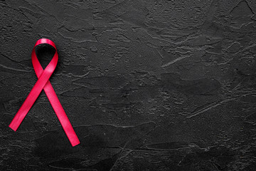 Red ribbon for HIV, AIDS, substance-abuse and anorexia awareness on black background top view copyspace